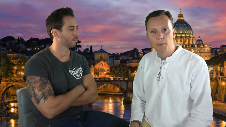 Jordi Wild, de brazos cruzados, y Daniel Pajuelo, que mira a cámara, sentados ante un fondo del Vaticano de noche.