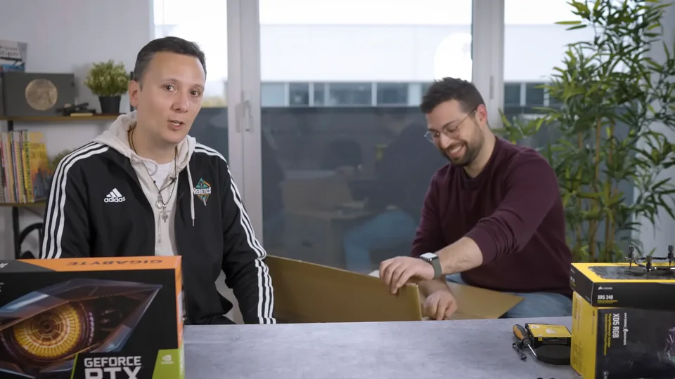 Daniel Pajuelo mira a cámara mientras Nate Gentile, sonriente, abre la caja del chasis del PC.