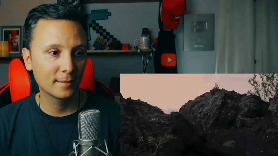 Daniel Pajuelo mira hacia abajo mientras comenta; a su lado, un paisaje rocoso del vídeo de Dama G