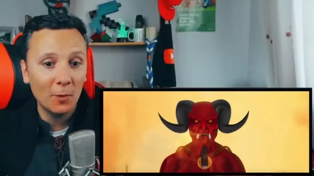 Daniel Pajuelo con sudadera negra y micrófono, mirando a cámara, con el diablo rojo del videoclip animado de «Es épico» en un recuadro. Análisis de «Es épico» de Canserbero.