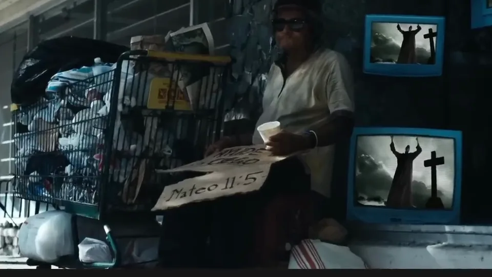 Un personaje del videoclip junto a un cartel con la referencia Mateo 11:5 y dos pantallas.